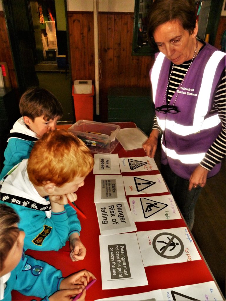 A woman stood next to a table with different saftey signs, children in scouting uniforms looking at the signs