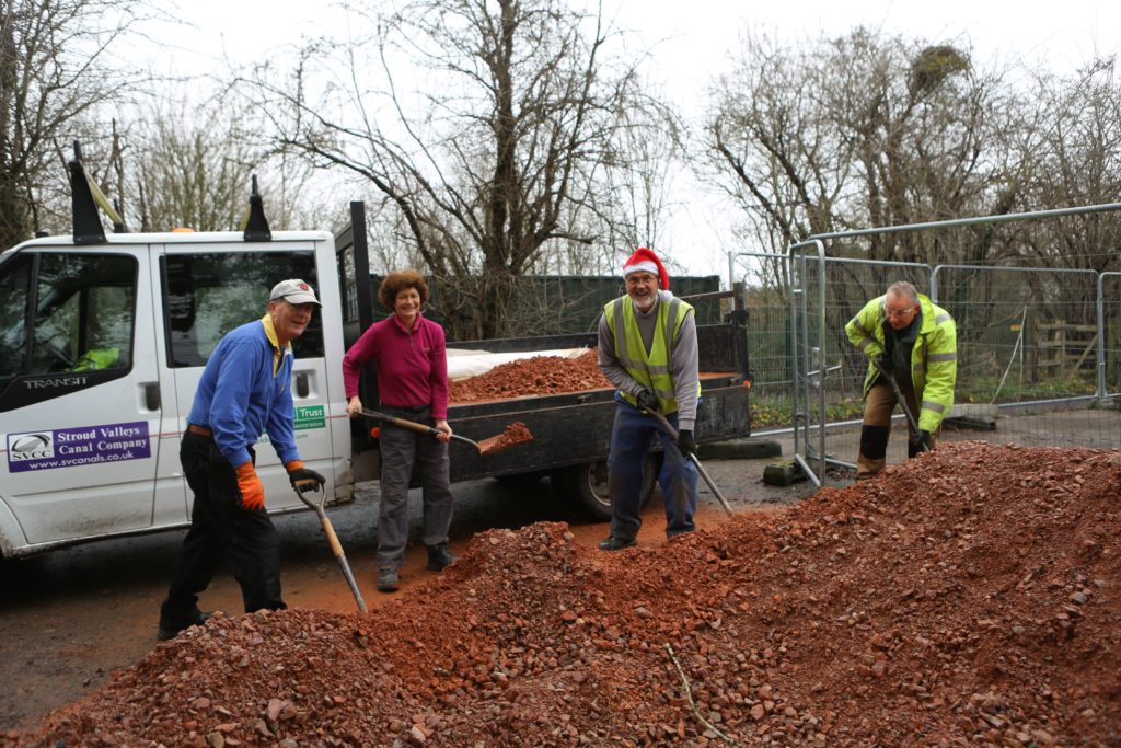 Four volunteers pictured shoveling gravel onto a truck. 